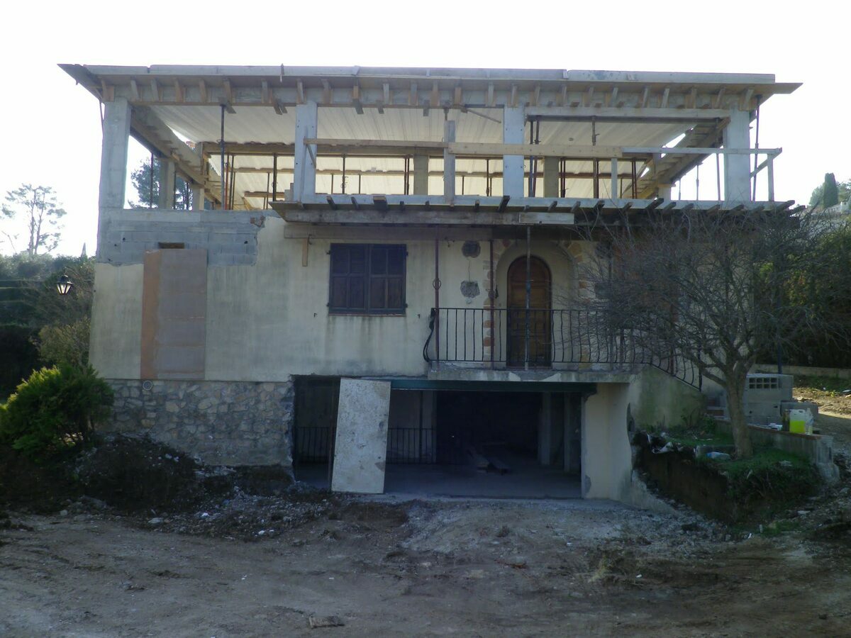 Rénovation lourde et surélévation d'une villa de 450 m² à Mougins Façade en pierre conservée d’une villa à Mougins surmontée de l’étage neuf en cours de structure